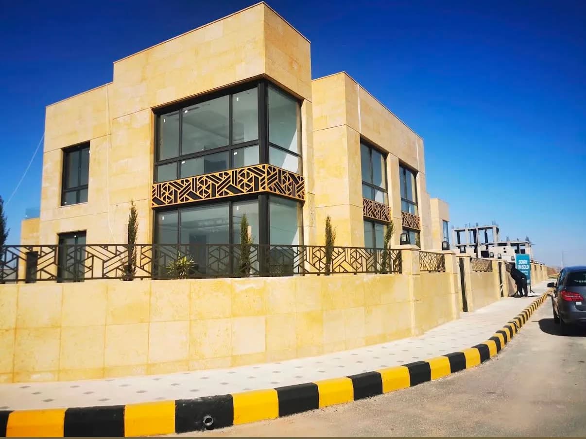 أول فيلا مكتملة في حوض العيادات — حجر بلون العسل وواجهة زجاجية ولافتة «بيعت» على السور